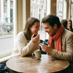 Twee mensen in levendig gesprek aan een houten cafétafel in Amsterdam, leunend naar elkaar met expressieve handgebaren en zachte daglichtsfeer.
